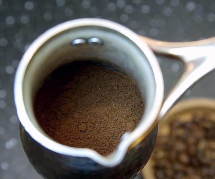 Приготовление кофе в турке. Шаг 2 − Засыпьте молотый кофе в турку и слегка потрясите, чтобы частицы легли равномернее.