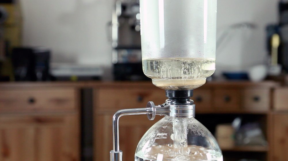 Приготовление кофе в сифоне. Шаг 6 − Когда вода начнет кипеть, установите верхнюю колбу, создав герметичное соединение с нижней. Вода должна подняться в верхнюю часть сифона